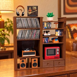 May include: A brown wooden media storage shelf featuring two tiers of vinyl records, a turntable, two speakers, and a side section with shelves holding cassette tapes, a miniature red television, a small plant, and a pair of headphones on a stand.