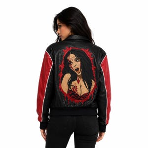 Peut inclure: Une veste en cuir noir avec des manches rouges et un passepoil blanc. Le dos présente une grande illustration graphique d'une personne aux longs cheveux noirs, semblant en détresse avec des éclaboussures rouges sur un fond noir.