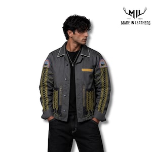 May include: A charcoal gray button-up jacket featuring olive green lace-up detailing along the sleeves and pockets, a pointed collar, and embroidered circular patches on the shoulders. The jacket includes a yellow rectangular chest accent and black trim.
