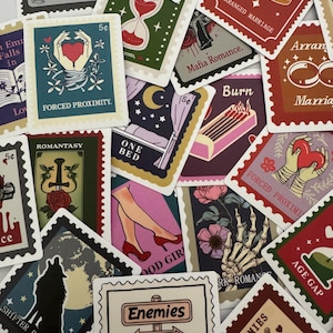 May include: A collection of decorative stickers with vintage postage stamp designs. The stickers feature various illustrations, including a heart, hourglass, and skeleton hand, with text such as "Burn," "Forced Proximity," and "Enemies to Lovers."