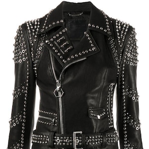 May include: Black leather jacket adorned with silver metal studs and eyelets. It has an asymmetrical zip, a notched collar, and a waist belt. The sleeves and shoulders are heavily embellished with studs and eyelets.