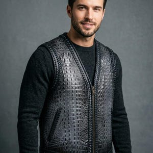 Peut inclure: Un gilet en cuir noir avec un motif peau de crocodile. Le gilet a une fermeture éclair et un col en V. Le modèle porte un pull gris foncé en dessous. Le gilet a une poche sur le côté gauche.