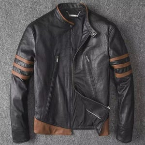 May include: Black leather jacket with brown detailing on the sleeves and hem. It has a stand-up collar, a zip closure, and two zipped pockets. The sleeves feature three brown stripes.
