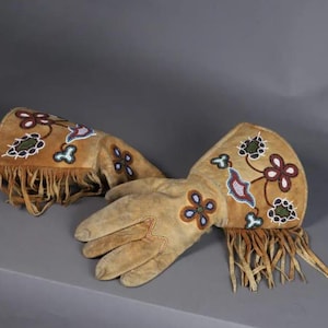 May include: A pair of tan suede gloves with floral beadwork and fringe. The gloves feature intricate bead designs in shades of blue, red, green, and white. The cuffs have long fringe.