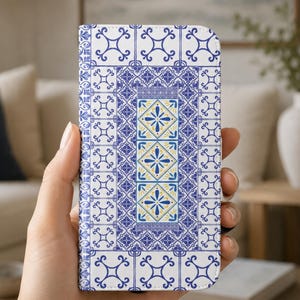 May include: A rectangular phone case featuring a white background with a repeating blue geometric tile pattern. The centre panel displays three vertical squares with blue and yellow floral motifs, framed by a border of intricate blue scrollwork.