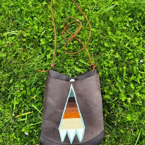 May include: A brown leather shoulder bag with a geometric design in shades of blue, orange, and white. The bag has a long brown strap.