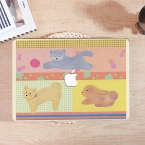 May include: A laptop protective cover featuring a multi-colored graphic design with a grey cat, a tan dog, and a brown rabbit. The background consists of horizontal bands in yellow, pink, and light green with polka dot patterns and a white Apple logo.