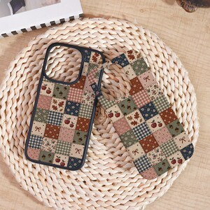 May include: A rectangular phone case featuring a patchwork design of squares with various patterns including red apples, brown acorns, small flowers, gingham checks, and bows in shades of sage green, navy blue, cream, and terracotta brown colors.
