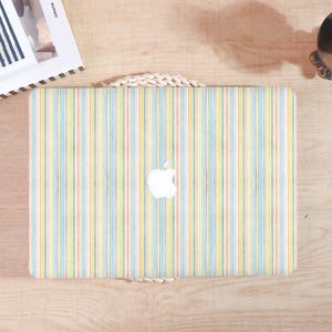 May include: A laptop with a colorful striped pattern in pastel shades of yellow, blue, and red. The Apple logo is visible on the laptop's surface. The laptop is placed on a light wooden surface.