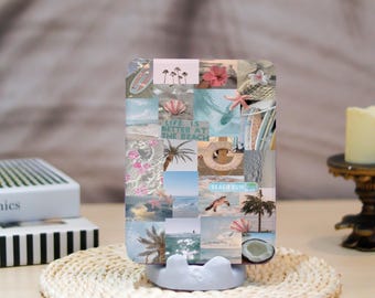 May include: A phone case with a collage of beach-themed images, including palm trees, seashells, and the text "Life is Better at the Beach." The case is displayed on a white stand, with a woven mat beneath.