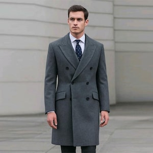 May include: A charcoal gray double-breasted overcoat. The coat features a notched lapel, two rows of buttons, and two front pockets. The person is wearing a white dress shirt and a navy blue patterned tie. The coat is knee-length.
