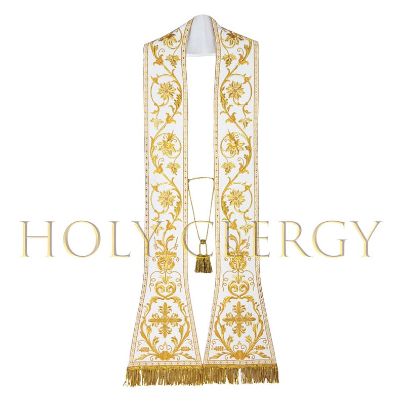 May include: White liturgical stole with gold floral embroidery and fringe. The stole features the text "HOLY CLERGY" in gold lettering. The design includes detailed floral patterns and a decorative tassel.