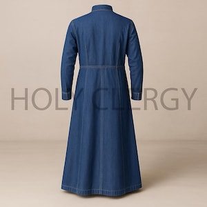 May include: A long, denim dress with long sleeves and a mandarin collar. The dress has a fitted waist and a flared skirt. The text "HOLY CLERGY" is visible in the background. The dress is made of a medium-wash denim fabric.