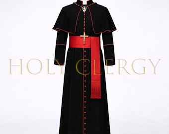May include: A black clergy robe with red trim, a red sash, and a cross pendant. The robe has long sleeves and a capelet. The text "HOLY CLERGY" is visible in gold lettering. The robe is displayed on a mannequin.