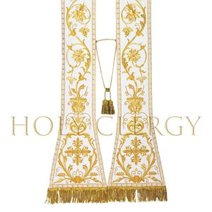 May include: White liturgical stole with gold floral embroidery and a gold tassel cord. The stole features intricate designs, including flowers and crosses, and is trimmed with a gold fringe. The word "HOLY CLERGY" is printed at the bottom of the stole.