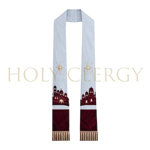 May include: A light blue clergy stole with a burgundy bottom section and gold fringe. The stole features a silhouette of a city with a star design. The text "HOLY CLERGY" is printed across the top.