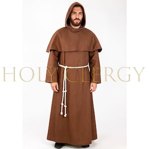 May include: A brown hooded robe with a matching cape and a white rope belt. The long-sleeved garment is worn by a person. The text "HOLY CLERGY" is visible in the background. The robe is made of a thick fabric.