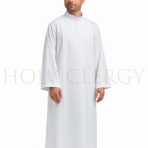 Puede incluir: Una túnica blanca de clérigo con mangas largas y cuello alto. La túnica tiene un diseño sencillo y elegante con un panel vertical en la parte delantera. El texto "HOLY CLERGY" es visible en la parte inferior de la imagen.