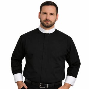 May include: Black long-sleeve shirt with a white collar and cuffs. The shirt has a button-down front and a chest pocket. The model is wearing a black belt and pants.