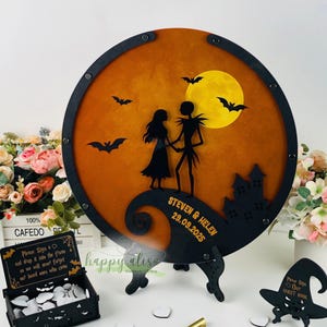 May include: A round, black wooden guest book alternative with a Halloween theme. It features a silhouette of a couple, bats, a full moon, and a castle against an orange and yellow background. The names "STEVEN & HELEN" and the date "29.09.2025" are inscribed.