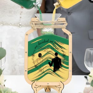 May include: A wooden sand ceremony set with a decorative jar-shaped frame. The frame holds layers of green and yellow sand, with the text "we decided on forever" and a couple illustration. The date 09.09.2024 is also displayed.