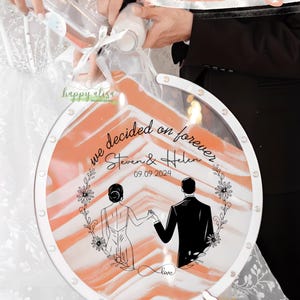 May include: A wedding sand ceremony set with a clear, circular container. The container has a white frame and a design of a couple holding hands. The text reads "we decided on forever" and the date "09.09.2024".