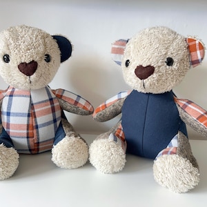 May include: Two plush teddy bears with beige fur, dark brown heart-shaped noses, and black eyes. One bear has navy blue ears and plaid arms and torso. The other bear has plaid ears and arms, and a navy blue torso. Both have fluffy white paws.