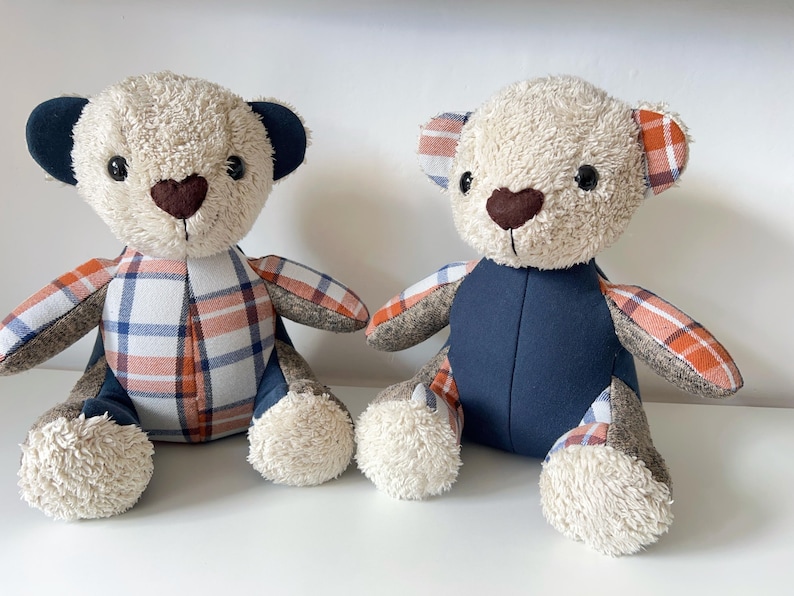 May include: Two plush teddy bears with beige fur, dark brown heart-shaped noses, and black eyes. One bear has navy blue ears and plaid arms and torso. The other bear has plaid ears and arms, and a navy blue torso. Both have fluffy white paws.