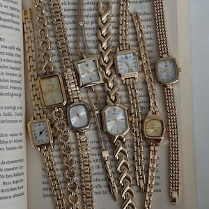 May include: A collection of eight gold-tone wristwatches with various link bracelet styles and rectangular, square, or hexagonal cases. Each watch features a white or metallic dial with hour markers and hands, arranged vertically on an open book page.