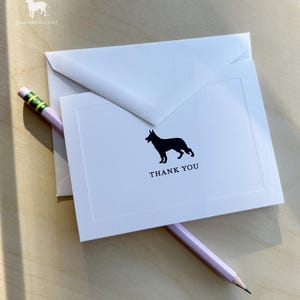 Puede incluir: Juego de papelería blanco con una silueta negra de un perro en una tarjeta que dice "GRACIAS". Un lápiz rosa con una goma verde descansa sobre la papelería. El logotipo de Oliver Blu es visible en la esquina superior izquierda.