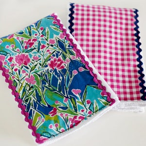 Könnte beinhalten: Zwei Küchentücher mit gewellten Rändern. Ein Handtuch hat ein rosa-weißes Karomuster, das andere ein Blumenmuster in Rosa, Blau und Grün.