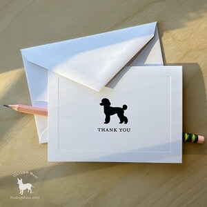 Puede incluir: Tarjeta de agradecimiento blanca con una silueta de caniche negro y la frase "THANK YOU". La tarjeta va acompañada de un sobre blanco y un lápiz rosa. Un juego de papelería.