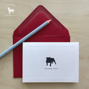 Puede incluir: Una tarjeta blanca con una silueta de bulldog negro y las palabras "THANK YOU" se combina con un sobre rojo y un lápiz gris. La tarjeta es parte de un juego de papelería. El logotipo de Oliver Blu está en la esquina superior izquierda.