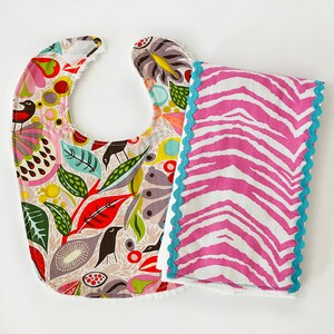 May include: A colorful bib with a floral pattern and a pink and white zebra print burp cloth with a turquoise trim.