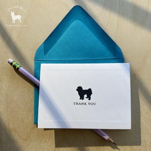 Puede incluir: Una tarjeta blanca con una silueta de perro negro y las palabras "THANK YOU" está dentro de un sobre turquesa. Un lápiz morado claro con una goma verde descansa sobre la tarjeta. El logotipo de Oliver Blu está en la esquina superior izquierda.