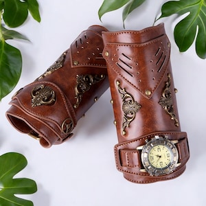 Peut inclure: Deux brassards steampunk en cuir marron avec des détails métalliques et une montre. Les brassards présentent des rivets décoratifs, des ornements métalliques et une montre intégrée. Le design évoque une esthétique vintage et industrielle. Mesure environ 20 cm.