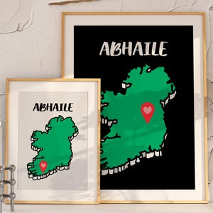 May include: Two framed art prints featuring a green map of Ireland with a red heart marker. The word "ABHAILE" is written in white above the map on a black background. One print is smaller than the other, both in gold frames.