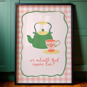 May include: Framed art print featuring a green teapot and a teacup with a floral design. The artwork is set against a pink and white checkered background, with the text "ar mhaith leat cupán tae?" in the lower portion.