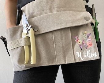 May include: Beige canvas gardening tool belt with multiple pockets and loops. Includes a pair of pruning shears and other tools. Features a floral "W" initial and the name "Willen" in script.