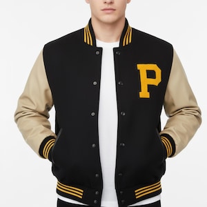 May include: Black varsity jacket with tan sleeves and a yellow "P" patch. The jacket has a black body, tan sleeves, and yellow and black striped trim on the collar, cuffs, and hem. It features a button-up front and pockets.