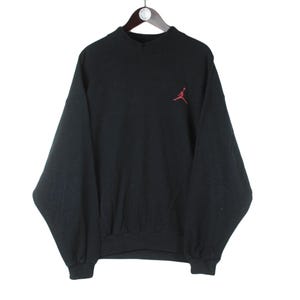 Może przedstawiać: Czarna bluza z czerwonym logo Jumpman z przodu.