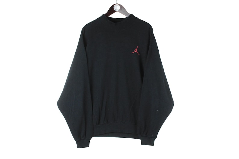 Może przedstawiać: Czarna bluza z czerwonym logo Jumpman z przodu.