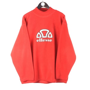 May include: A bright red long-sleeve fleece pullover featuring a mock neck collar. The center of the chest displays the white ellesse logo with its signature semi-circle graphic above the brand name in a lowercase serif font.
