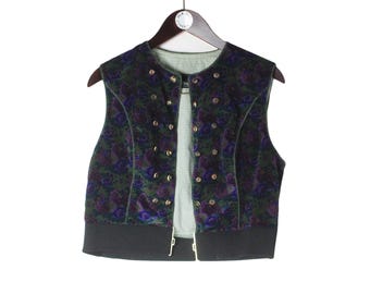 Op de afbeelding: Een vintage vest met bloemenpatroon in groen, paars en zwart. Het vest heeft een zwarte zoom en is gevoerd met een lichtgroene en wit geruite stof. Het heeft meerdere goudkleurige knopen. Het vest hangt aan een houten kleerhanger.