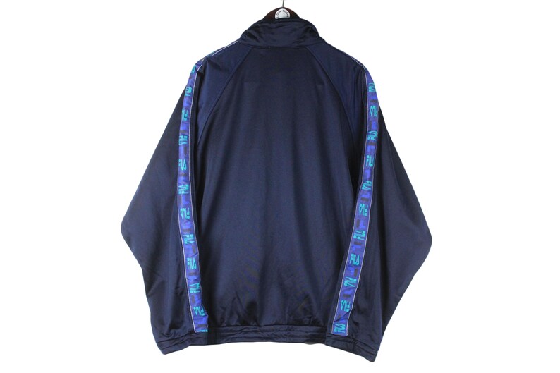 Puede incluir: Una chaqueta de ch&aacute;ndal azul marino con cierre de cremallera y ribetes blancos. La chaqueta tiene ribetes azules y morados con texto repetido a lo largo de las mangas y los lados.