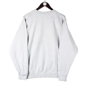 Puede incluir: Una sudadera gris con mangas largas y cuello redondo.