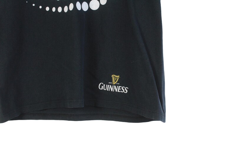 Pu&ograve; includere: T-shirt nero con un motivo a pois bianchi nella parte superiore. Il logo Guinness, con un'arpa e la scritta "Guinness", &egrave; stampato in oro e bianco in basso a destra. La maglietta &egrave; realizzata in un materiale morbido.