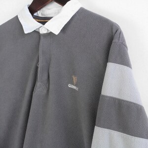 Puede incluir: Camisa de rugby gris de manga larga con cuello blanco y mangas a rayas grises claras. Cuenta con el logotipo de Guinness bordado en el pecho. La camisa est&aacute; hecha de una tela suave y texturizada.