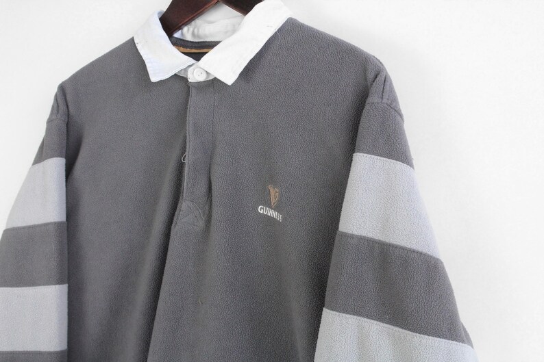 Puede incluir: Camisa de rugby gris de manga larga con cuello blanco y mangas a rayas grises claras. Cuenta con el logotipo de Guinness bordado en el pecho. La camisa est&aacute; hecha de una tela suave y texturizada.