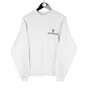 May include: White sweatshirt with the Guinness logo on the upper left chest. The long-sleeved crew neck shirt is hanging on a black hanger against a white background. The Guinness logo features a black harp and the Guinness wordmark.